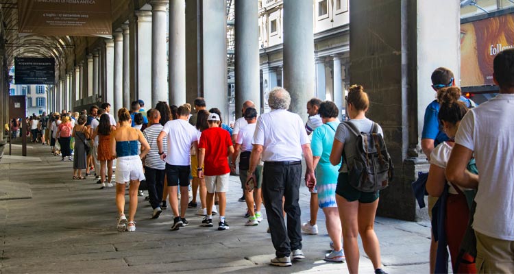 Crowd of tourists waiting in line under the arches of the Uffizi Gallery in Florence, Italy, on a sunny day.